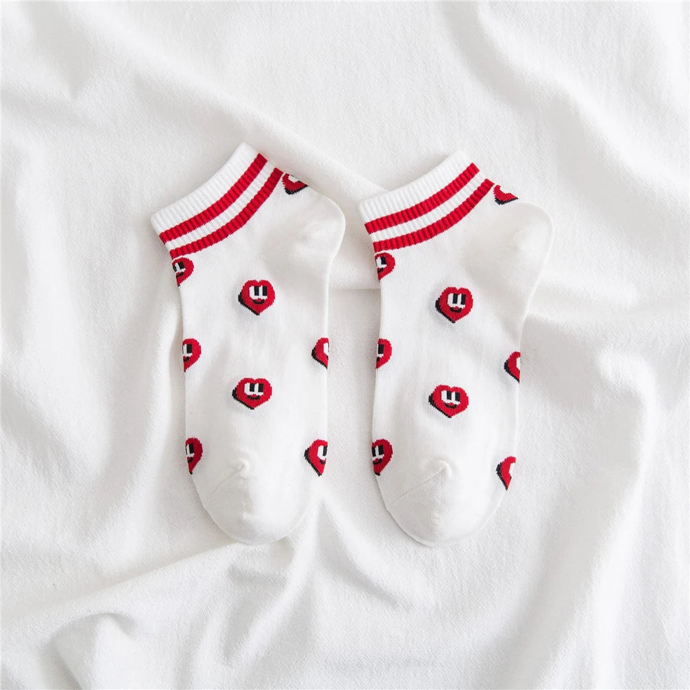 A pair of white striped socks with red heart patterns on the toes and red trim.