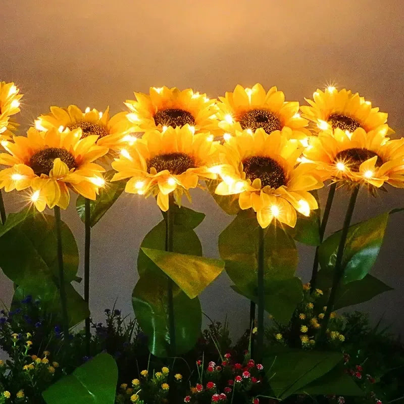 Three solar sunflower LED stake lights with bright yellow blooms and green leaves against a dark background.