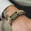 A close-up of a tactical paracord bracelet with a black flag charm featuring the American flag design on a person's wrist.