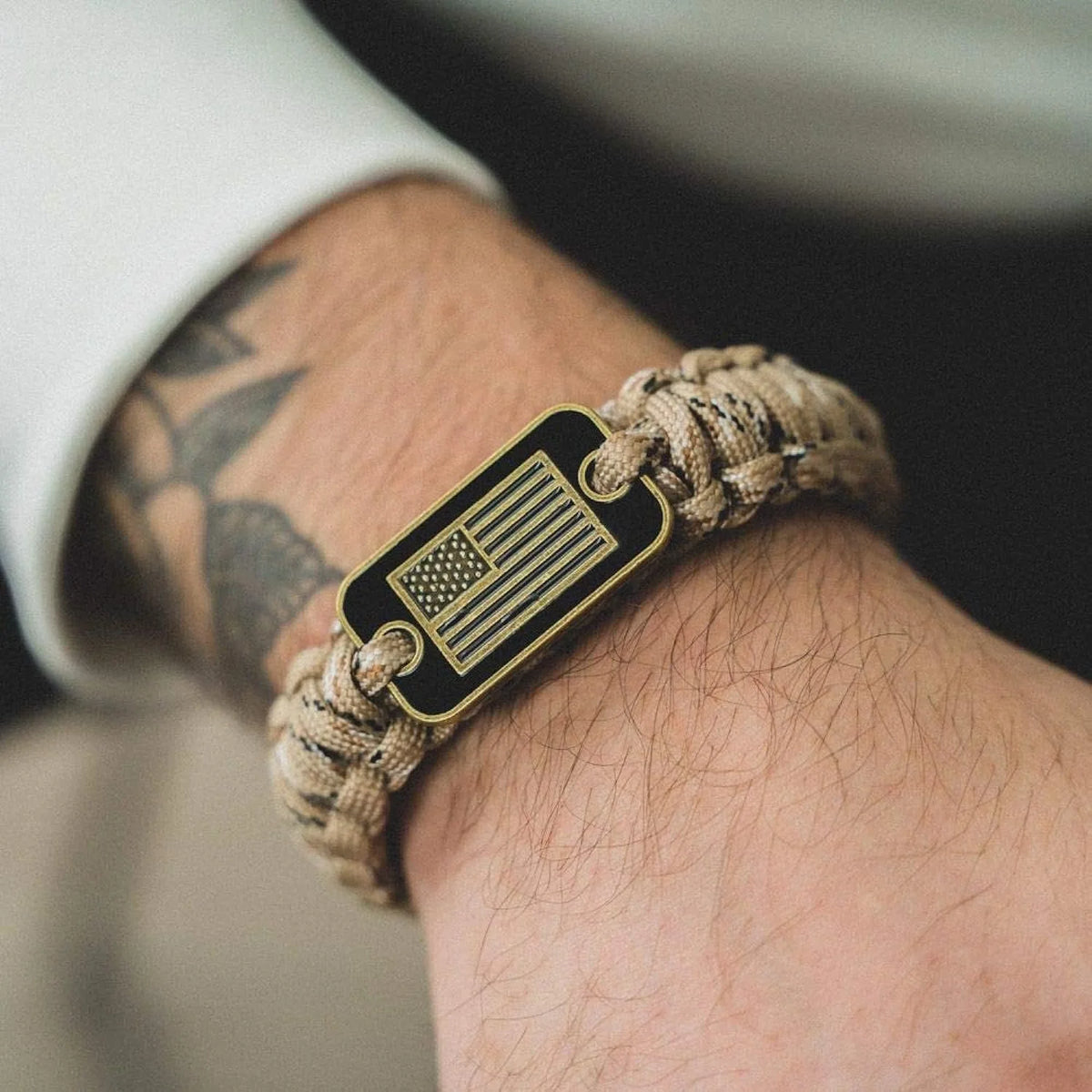 A close-up of a tactical paracord bracelet with a black flag charm featuring the American flag design on a person's wrist.