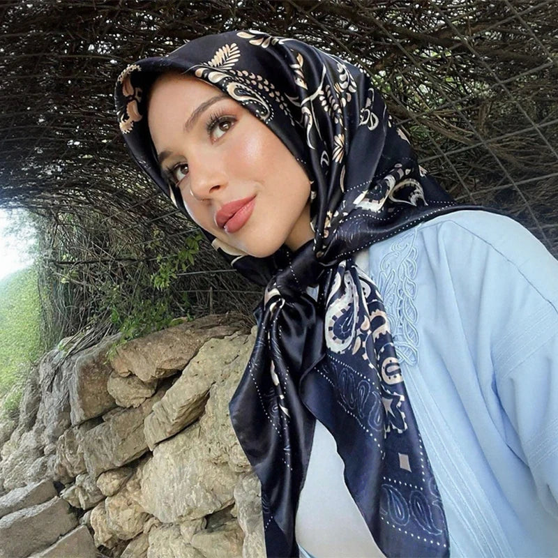 A woman wearing an elegant black and white patterned satin square scarf hijab looking towards the camera.