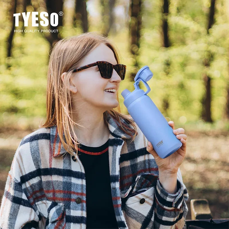 Une jeune femme portant des lunettes tient une tasse isotherme en acier inoxydable bleue à l'extérieur.