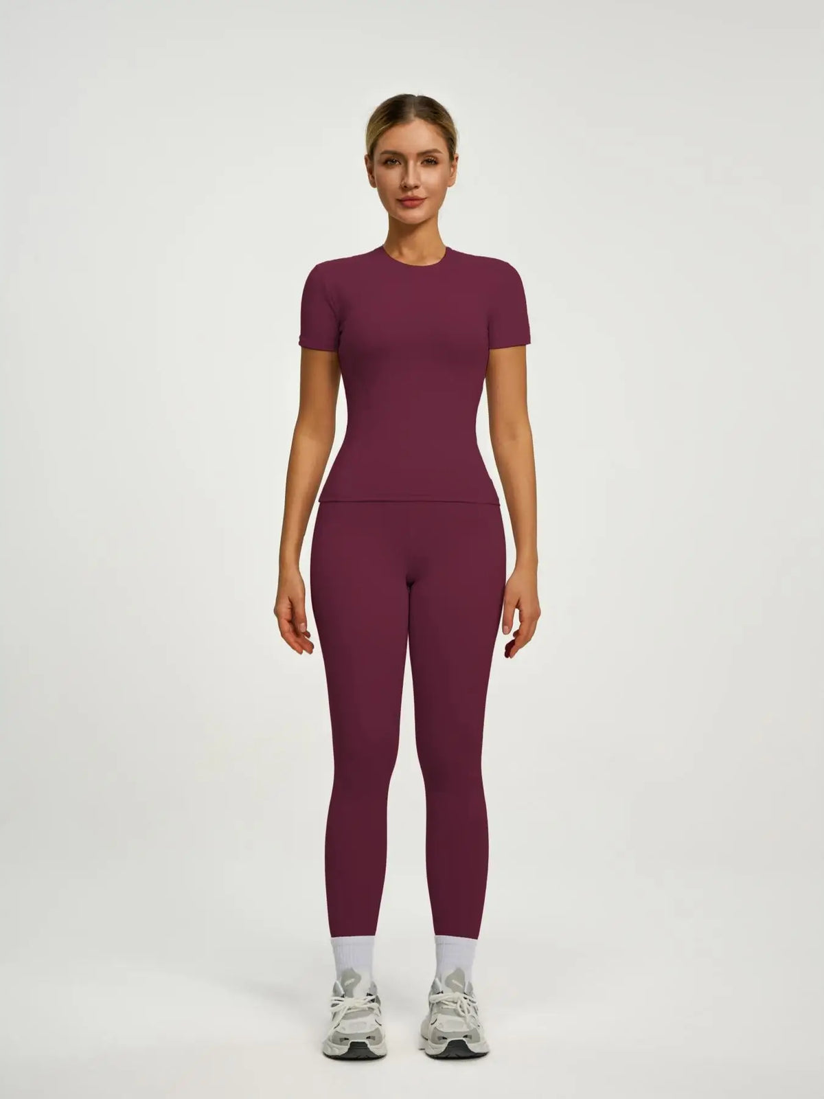 Model trägt ein sportliches Yoga-Set in tiefem Pflaum, bestehend aus einem kurzärmeligen Oberteil und langen Leggings.