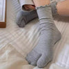 Gray knit crew socks with ruffle cuffs being worn on a foot.