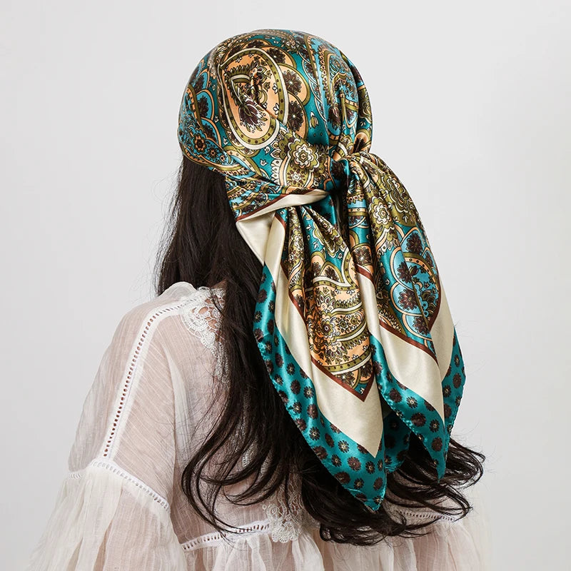 A woman wearing a teal and gold paisley silk shawl scarf tied around her neck, visible over a sheer white top.