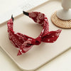 Accesorio para el cabello de tela roja estampada atado en lazo, exhibido sobre una superficie clara.