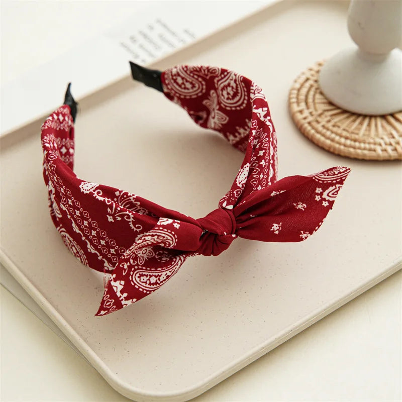 Accesorio para el cabello de tela roja estampada atado en lazo, exhibido sobre una superficie clara.