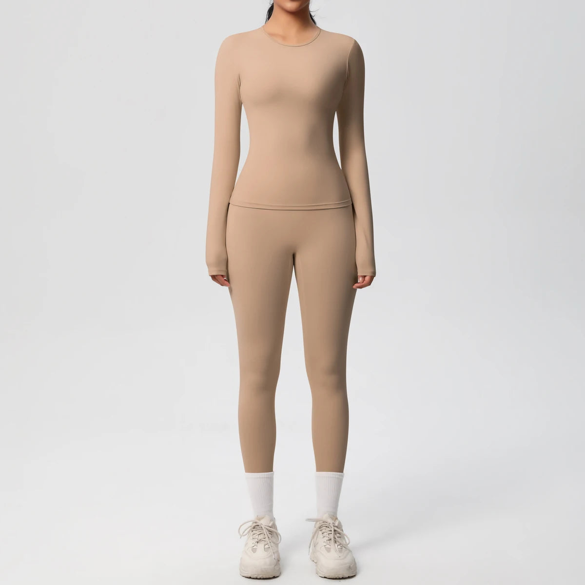 A woman wearing a long-sleeved, fitted beige performance yoga and gym set with matching leggings and shoes.