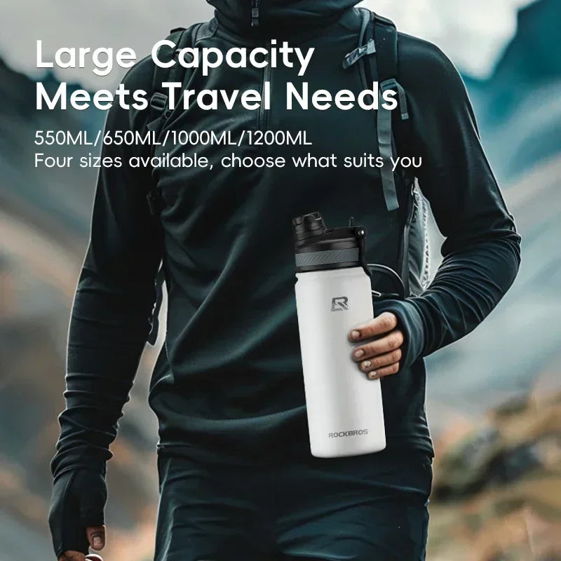 A person wearing a black hoodie holds a white insulated water bottle outdoors.