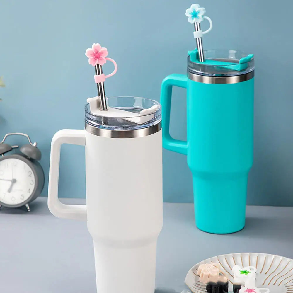 A white silicone butterfly straw cover is shown on a tumbler, with a teal mug featuring a matching straw and flower topper.
