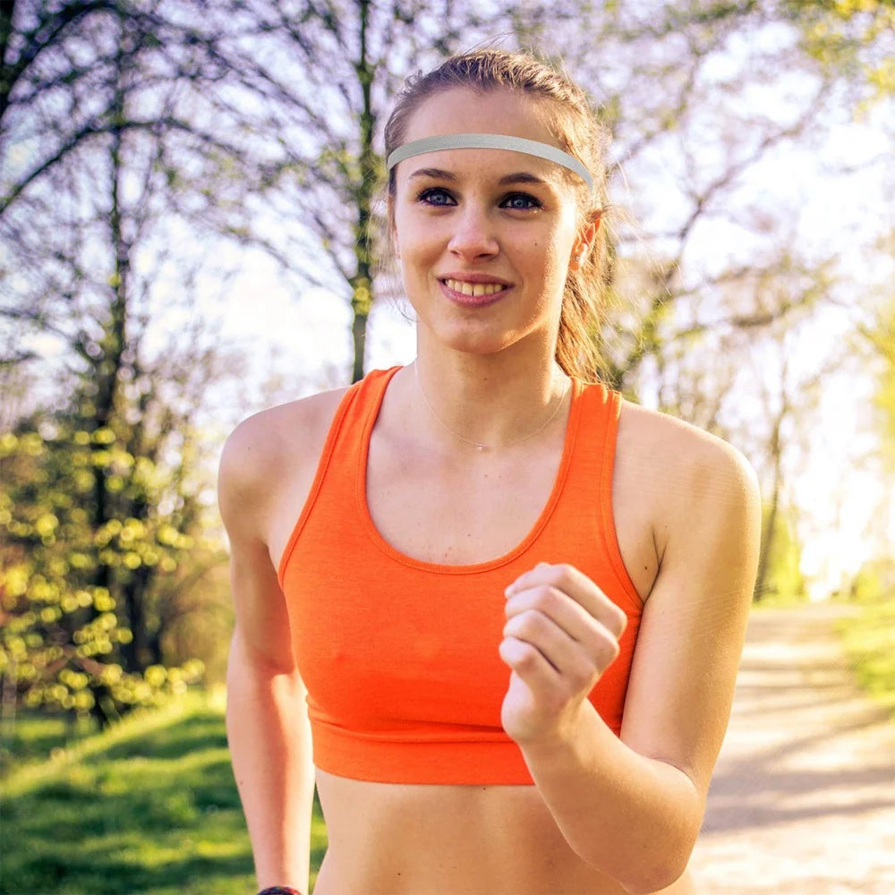 Eine junge Frau in einem orangefarbenen Sporttop und einem Stirnband läuft auf einem Erdweg im Freien.
