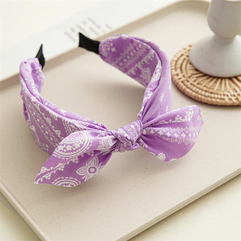 Accesorio para el cabello de tela estampada morada atado en un lazo, exhibido sobre una superficie clara.