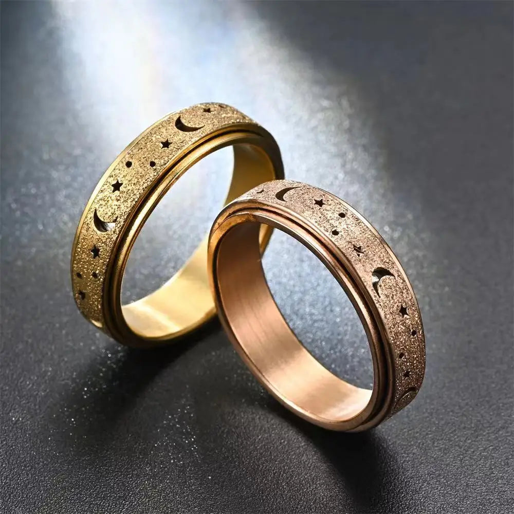 Two gold-toned stainless steel spinning rings featuring moon and star designs on a dark surface.