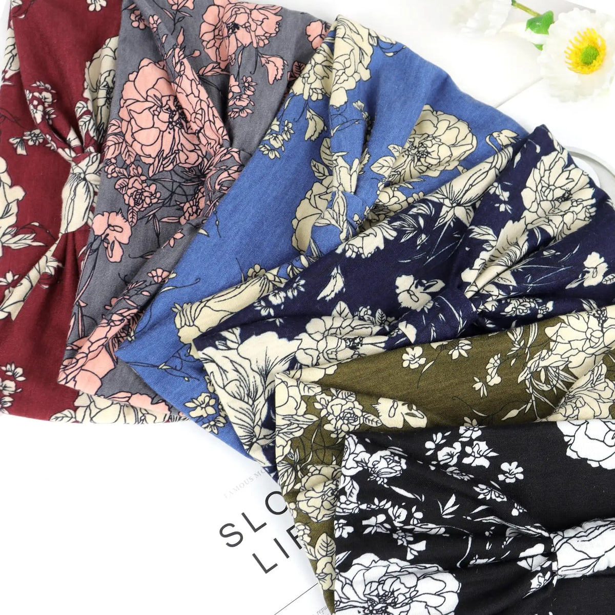 Collection de bandeaux de tête en coton élastique à motifs floraux colorés style bohème, disposés sur une surface blanche.
