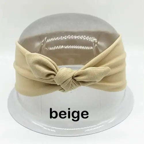 Beige Stoff-Haarband, gebunden in eine Schleife, auf einem weißen runden Ständer.