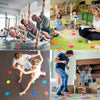 Kinder spielen auf einer farbenfrohen Matte mit Sitzmarkern und Bausteinen in einem Klassenzimmer.