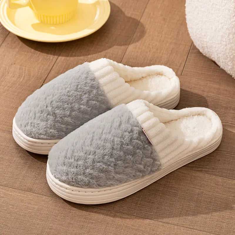 Gray and cream plush fleece slippers resting on a wooden surface with a yellow plate nearby.