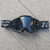 Une paire de lunettes de moto tout-terrain et ATV noires posées sur une surface grise texturée.