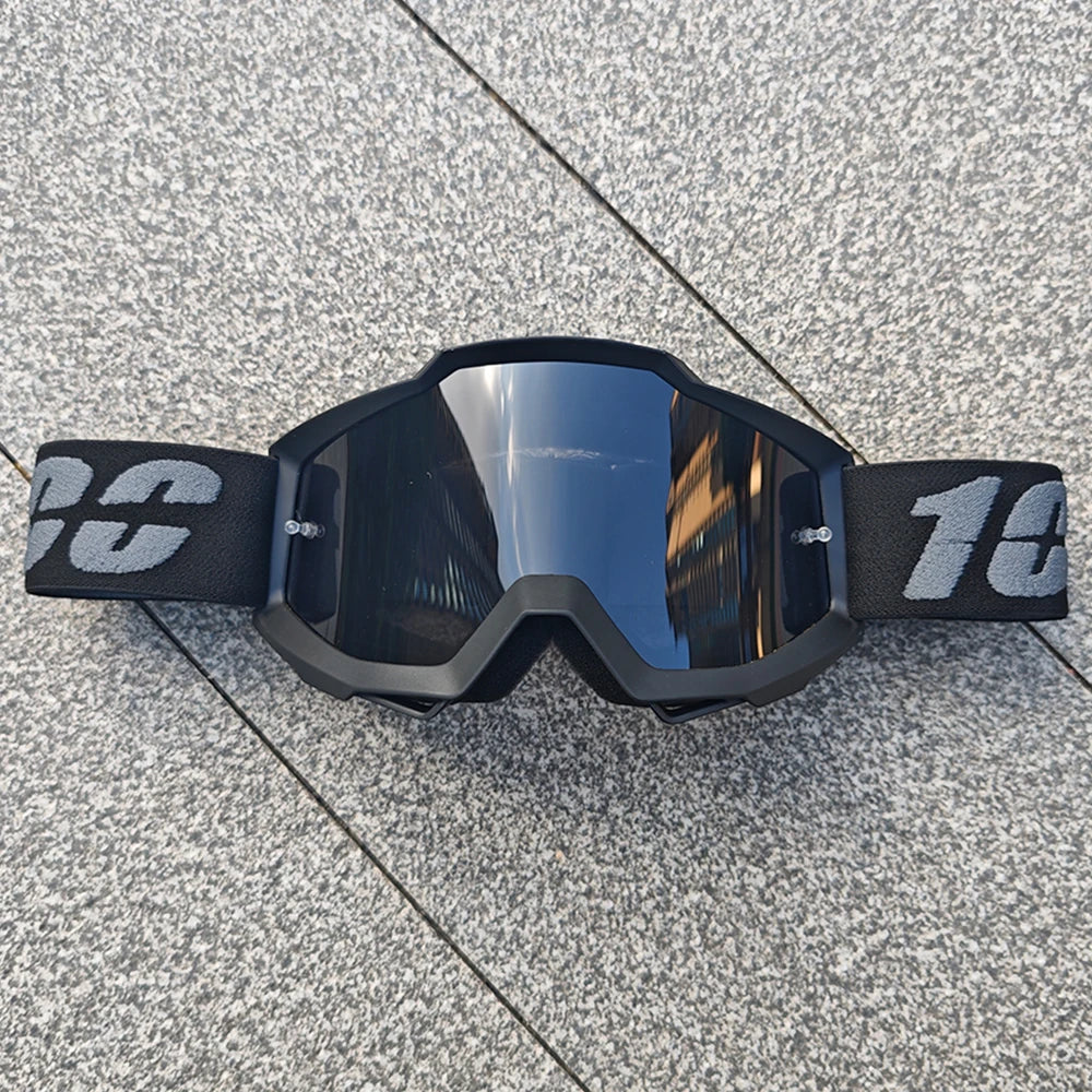 Une paire de lunettes de moto tout-terrain et ATV noires posées sur une surface grise texturée.