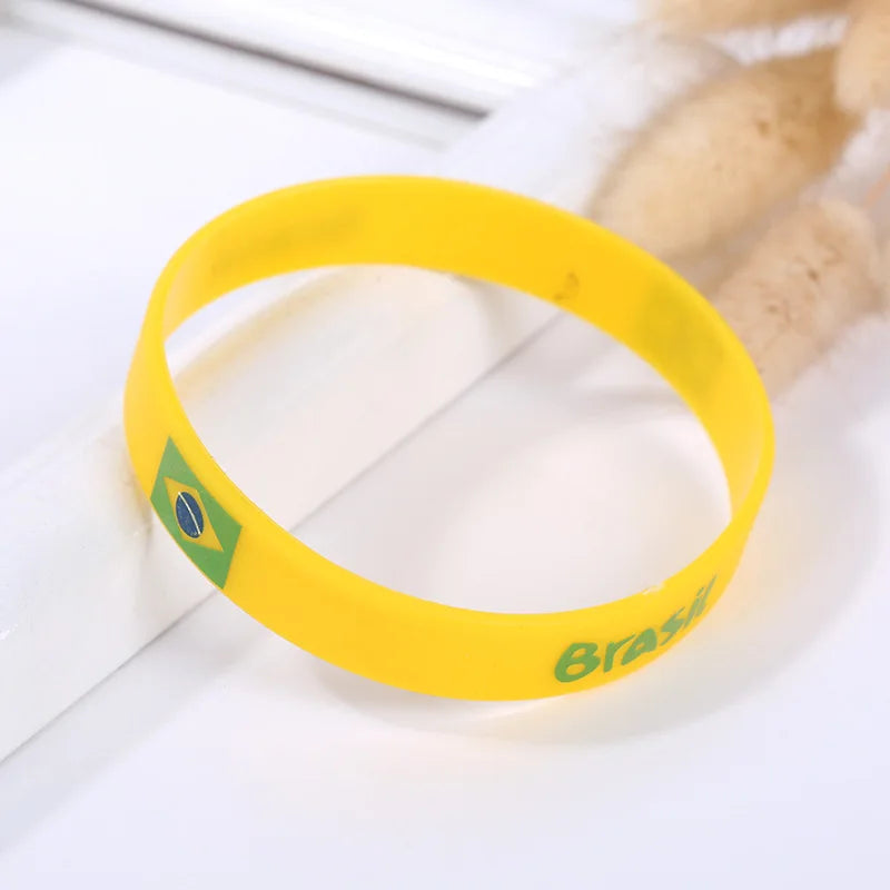 Yellow silicone wristband with the Brazilian flag design resting on a white surface.