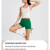 A woman wearing a white sports bra and green yoga shorts with a dark cap and white socks.