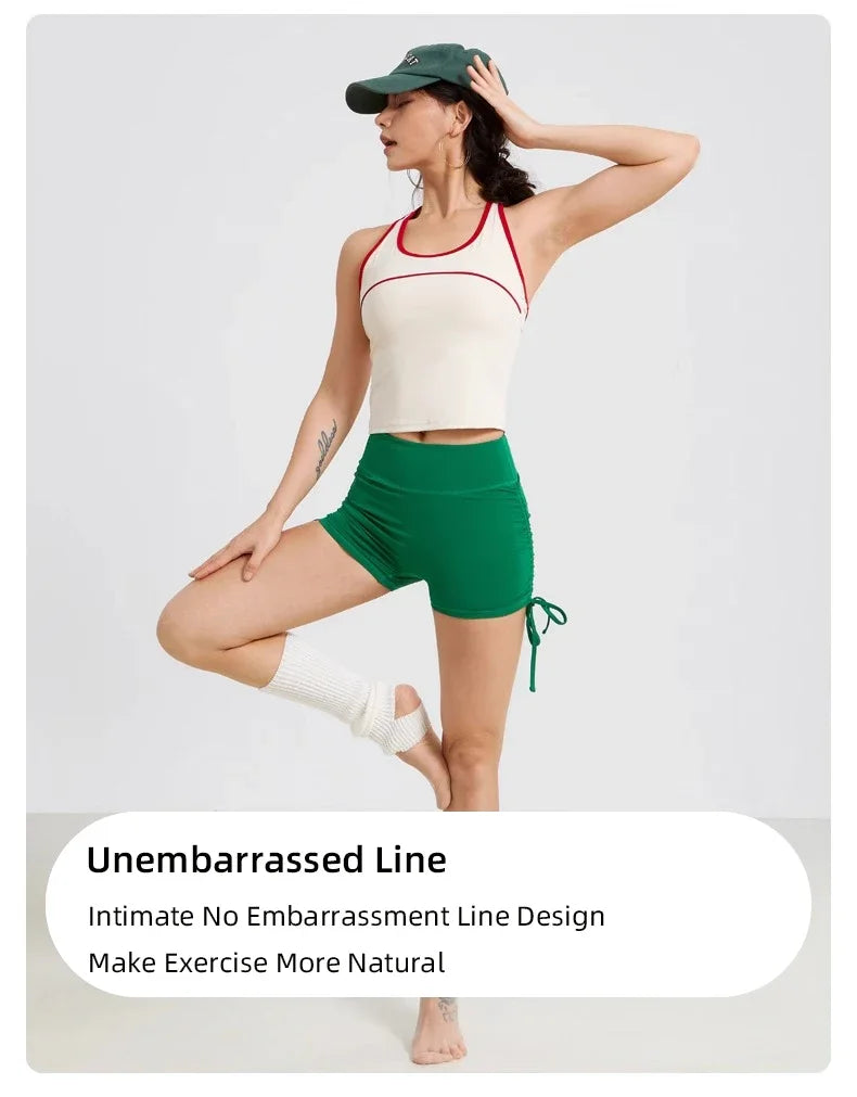 A woman wearing a white sports bra and green yoga shorts with a dark cap and white socks.
