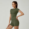 Una mujer modela un conjunto de yoga verde oliva de cintura alta con top de manga corta y shorts a juego.
