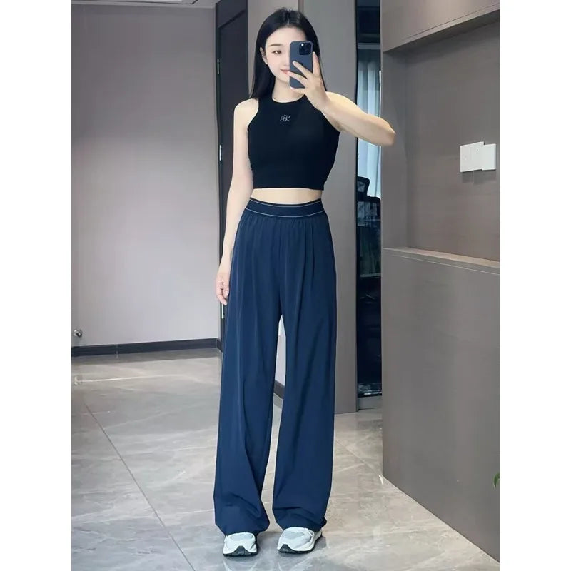 A woman models dark blue loose sports yoga pants and a black crop top in an indoor setting.