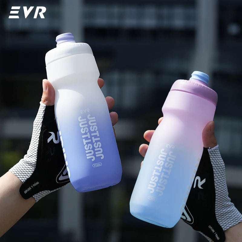 A hand holds a light purple cycling water bottle with a white cap against a blurred outdoor background.
