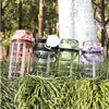 A collection of clear water bottles with various colored lids and a white light, resting on green foliage.