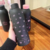 Una mano sostiene una taza de viaje de acero inoxidable doble pared gris oscuro con detalles rosas sobre una superficie de ma