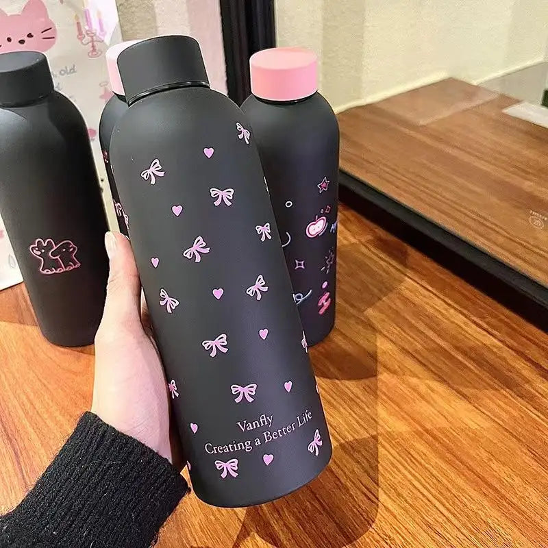 Una mano sostiene una taza de viaje de acero inoxidable doble pared gris oscuro con detalles rosas sobre una superficie de ma