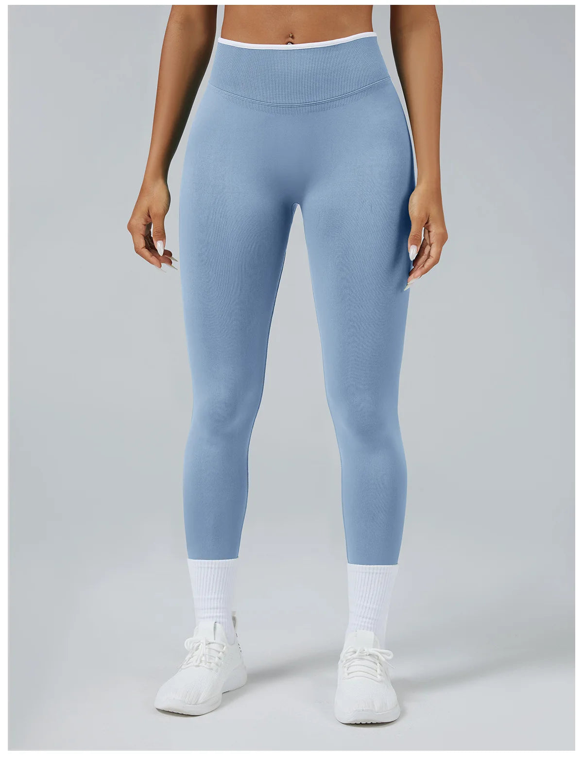A woman wearing light blue high-waist yoga leggings and white socks standing against a plain background.