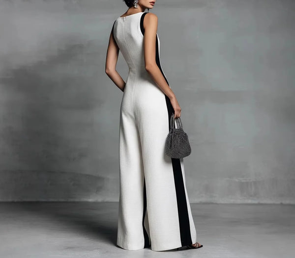 A woman wearing a white and black color block jumpsuit with a V-neck and pockets, standing against a gray background.