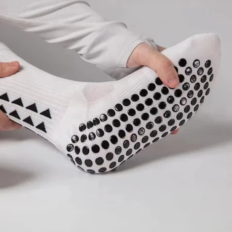 A close-up of white athletic grip socks being held by a hand, showing the textured pattern.