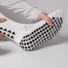 A close-up of white athletic grip socks with black studs and mesh texture being held by a hand.