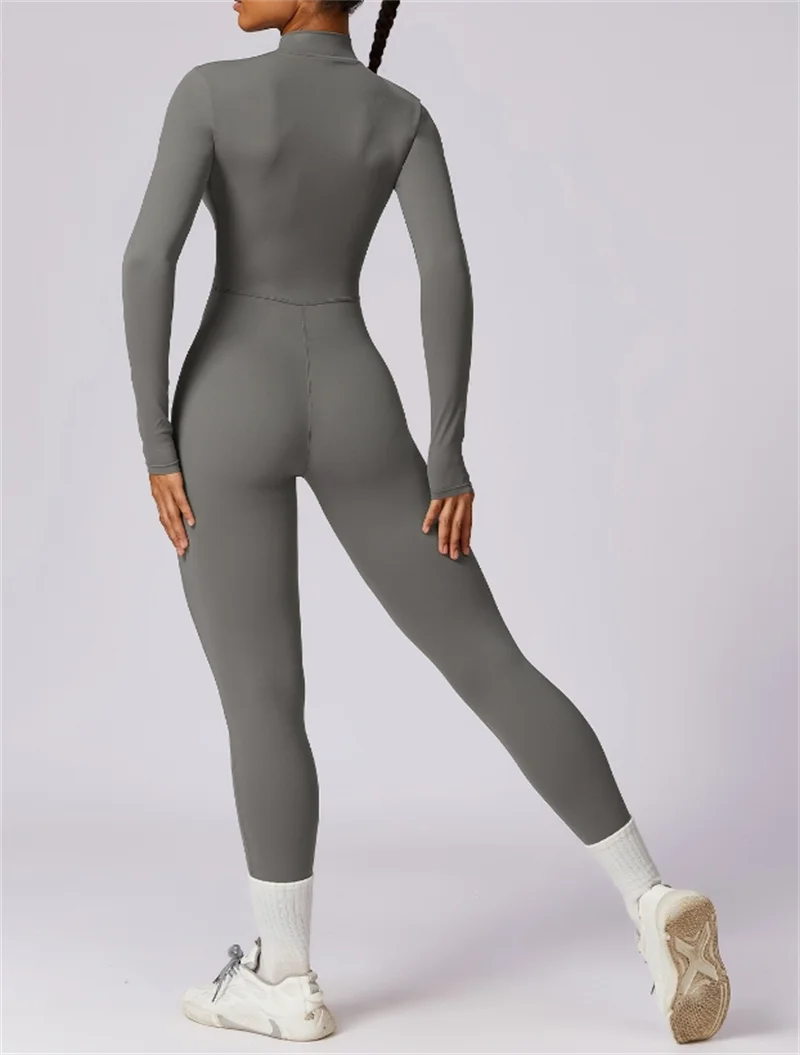 Model trägt einen figurbetonten, langärmeligen grauen Yoga-Jumpsuit mit hohem Kragen und Langhosen.