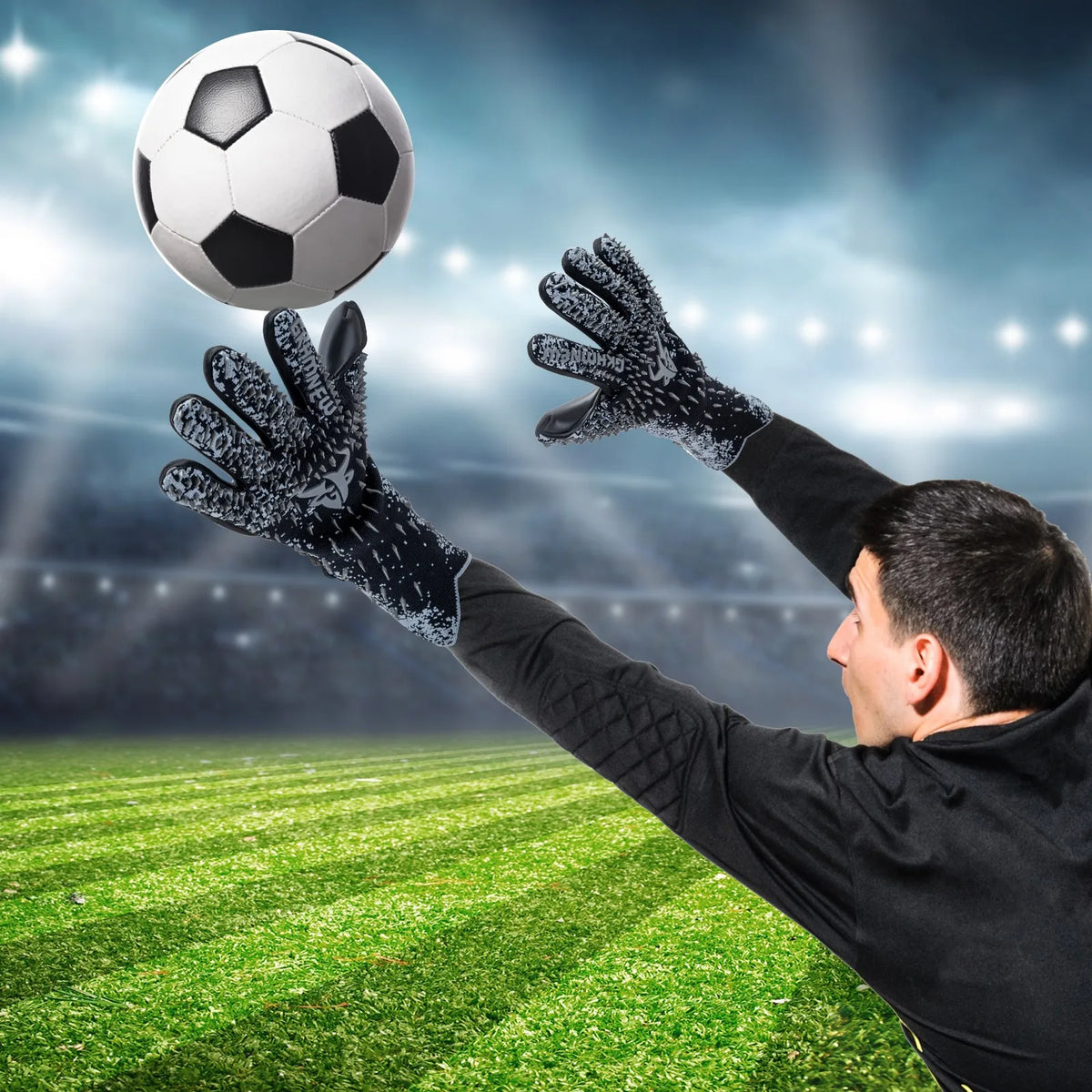 A male goalkeeper wearing black gloves catches a soccer ball against a bright, stadium-like background.