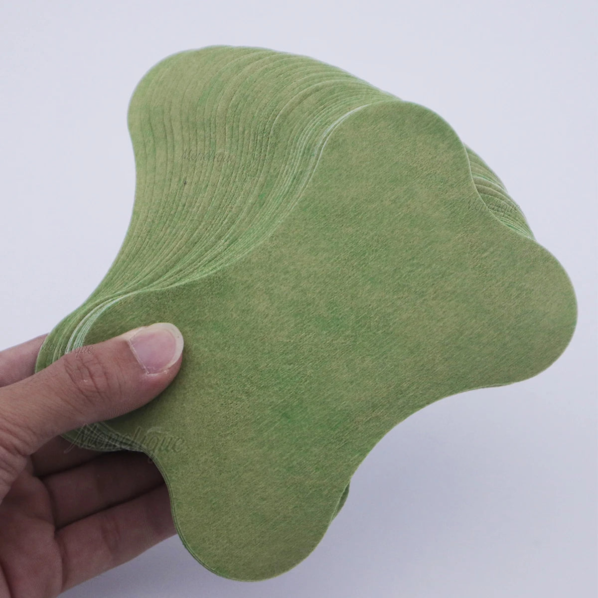 A hand holds a light green self-heating lumbar spine patch, showing its contoured shape.