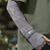 Gros plan d'une personne portant des manches de protection UPF 50+ grises à motifs sous une veste vert olive.