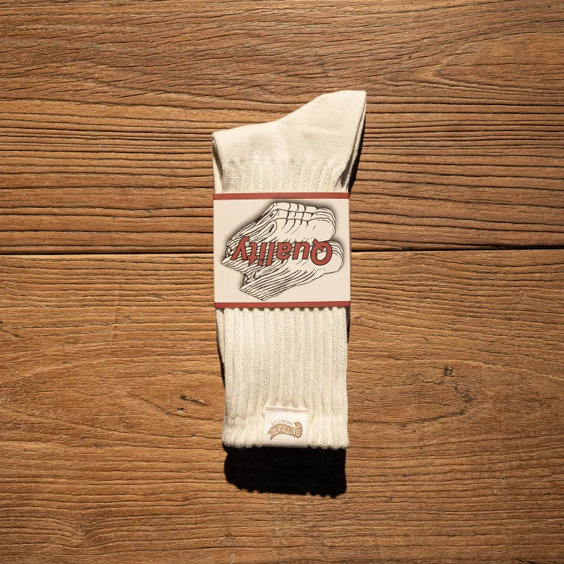 A pair of beige tube socks with a red and white logo band lying on a wooden surface.