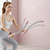 A woman is demonstrating adjustable ropeless battle ropes for home fitness exercise against a pink wall.