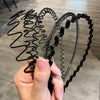 A hand is holding a black fashion metal hair band with a coiled design.