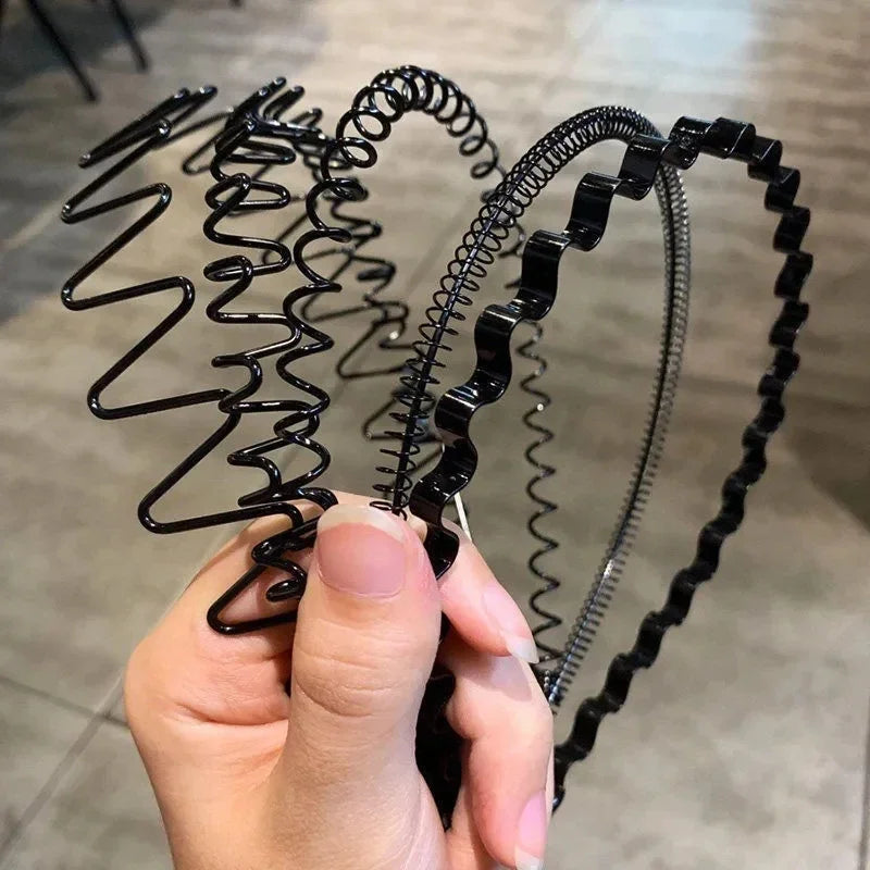 A hand is holding a black fashion metal hair band with a coiled design.