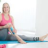 A woman demonstrates using synthetic kinesiology therapy tape on her leg while stretching on a blue mat.
