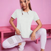 A woman wearing a white breathable summer yoga and fitness t-shirt and white leggings sitting on a pink bench.