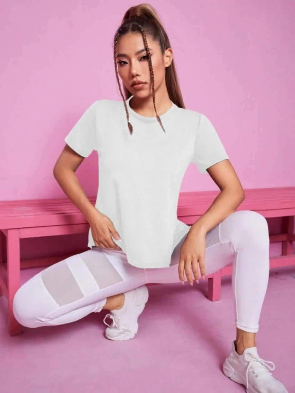 A woman wearing a white breathable summer yoga and fitness t-shirt and white leggings sitting on a pink bench.