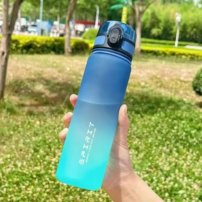 A hand holds a gradient blue insulated sports water bottle outdoors on a grassy area.