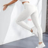 Une femme portant des leggings de yoga en tricot uni blancs, appuyée contre un mur blanc.