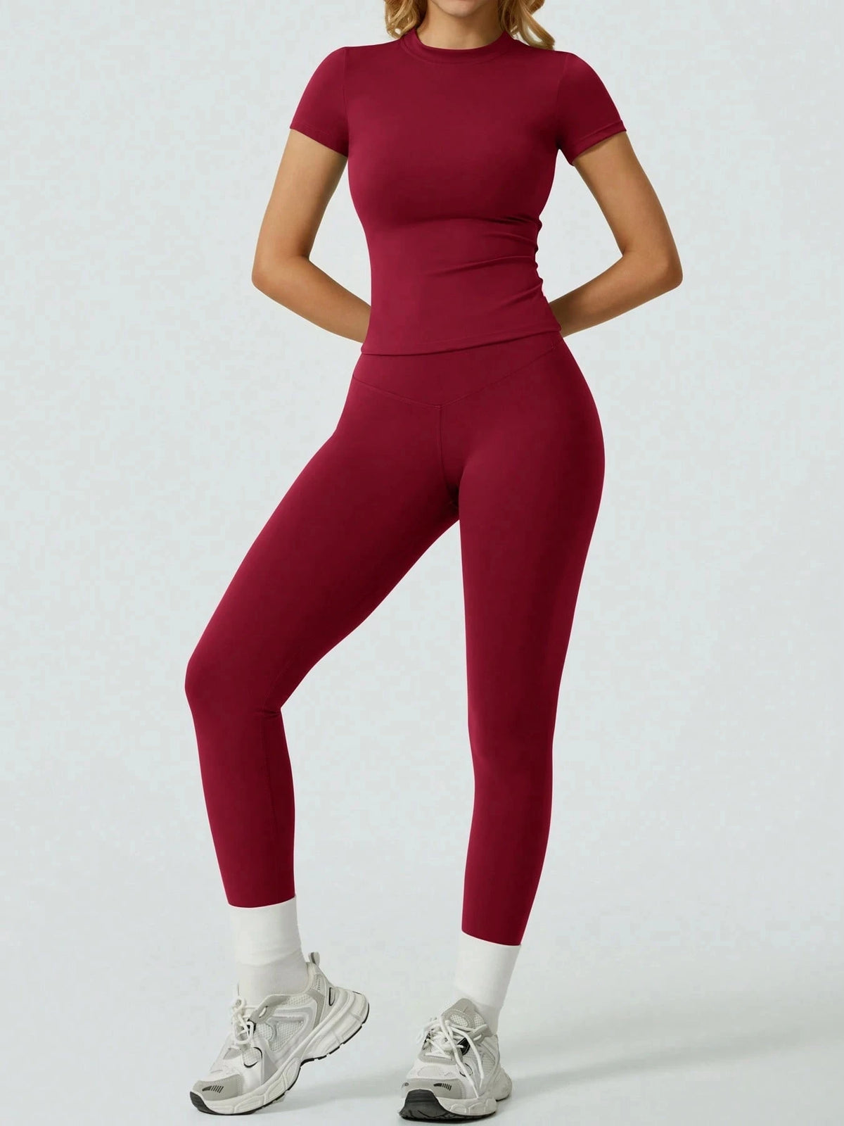 Eine Frau trägt ein dunkelrotes Yoga-Set mit hohen Bund-Leggings und einem kurzen Top.